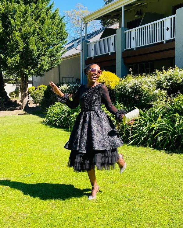 Woman wearing a black jacquard party dress with sheer sleeves and tulle hem on a garden lawn
