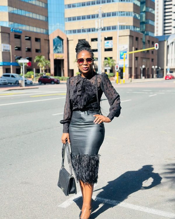 Woman in a sheer black polka-dot bow blouse and black leather-look pencil skirt with feather hem