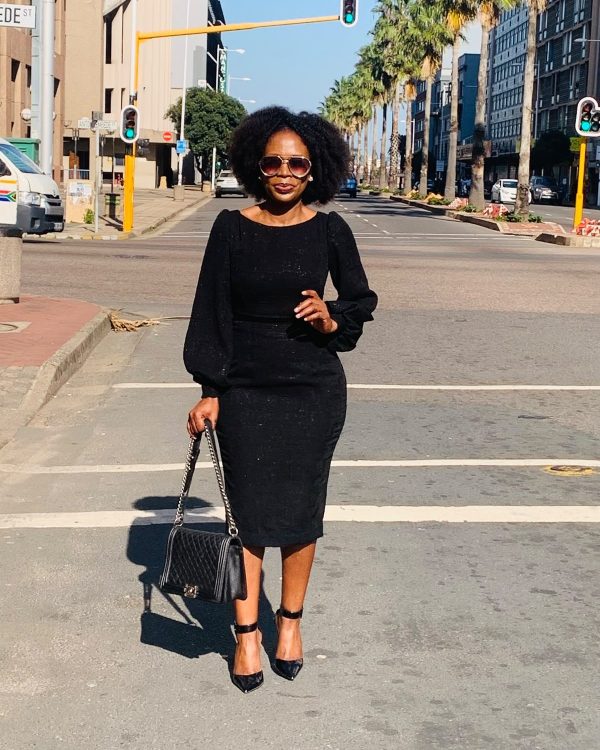 Woman in a fitted black textured midi dress with bishop sleeves on a city street