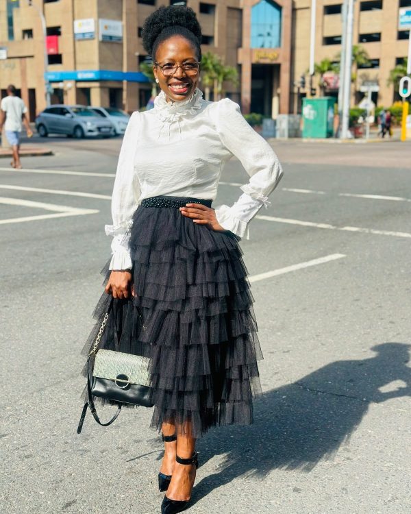 Woman in a black tiered tulle midi skirt with a white high-neck ruffle-cuff blouse