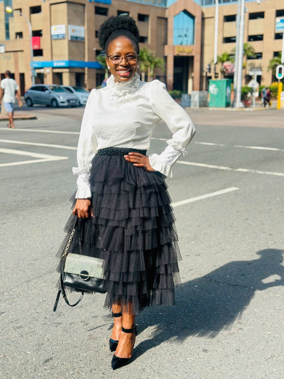 Woman in a black tiered tulle midi skirt with a white high-neck ruffle-cuff blouse