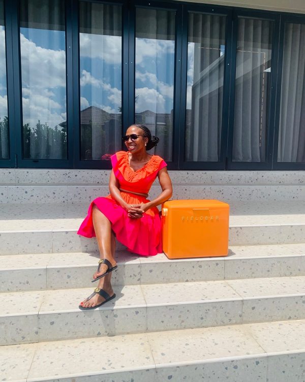 Woman sitting on steps in a coral midi dress with ruffled neckline and belted waist