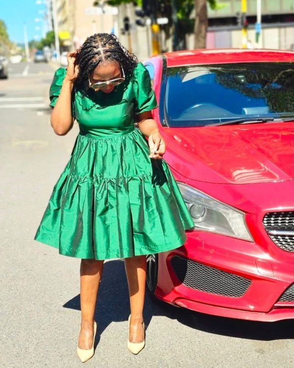 Woman in an emerald green tiered dress with puff sleeves standing beside a red car