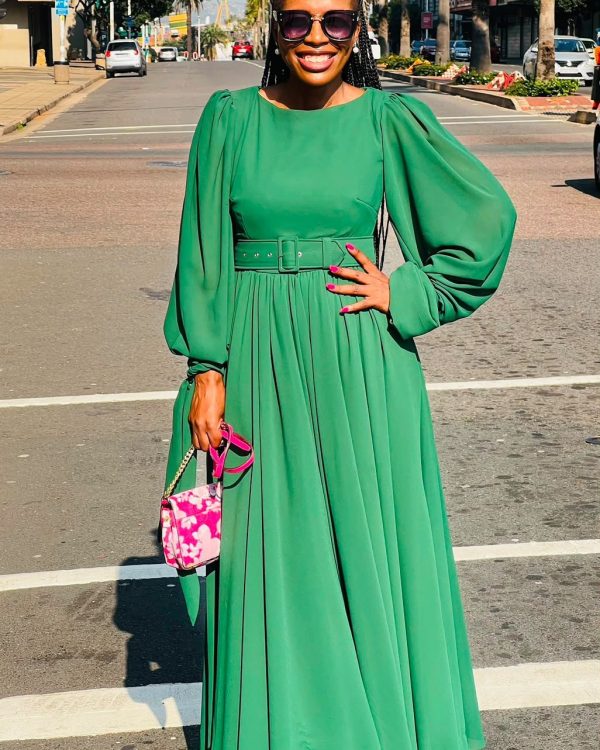 Woman in a green belted chiffon maxi dress with balloon sleeves holding a pink handbag