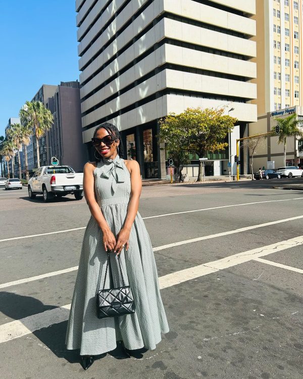 Woman in a grey halter-neck maxi dress with bow at the neck holding a black quilted bag