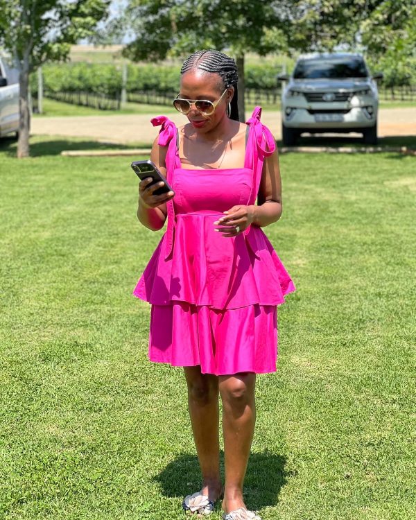 Woman in a hot pink tiered dress with tie shoulder straps standing on grass
