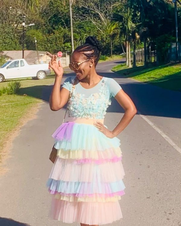 Woman in a pastel rainbow tiered tulle dress with floral appliqué bodice on a tree-lined street