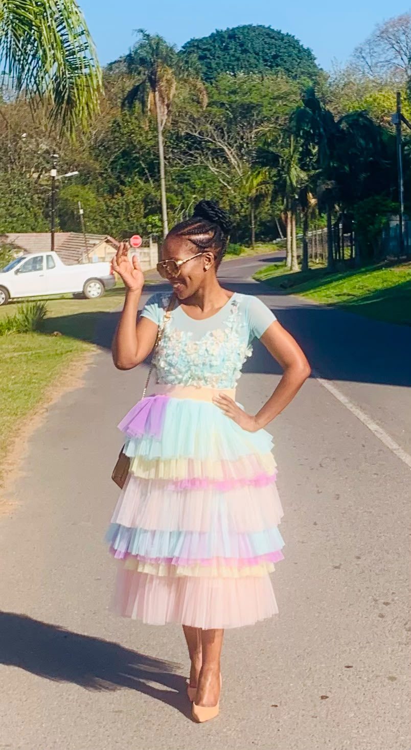 Woman in a pastel rainbow tiered tulle dress with floral appliqué bodice on a tree-lined street