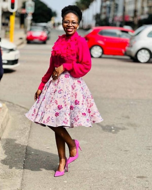 Smiling woman in a hot pink ruffle blouse and full pink floral midi skirt with pink heels