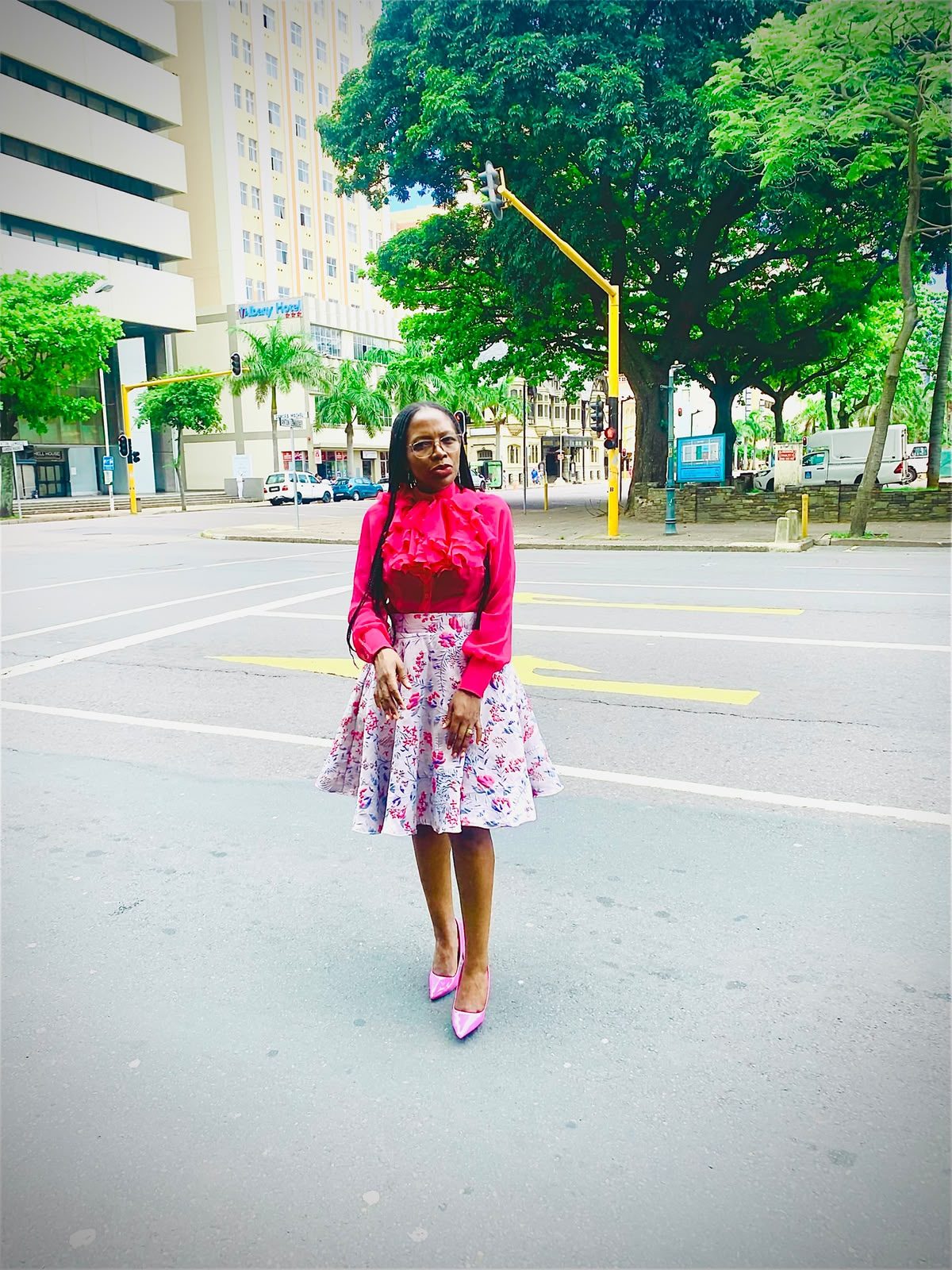 Woman in a hot pink ruffle blouse and pink floral skirt standing on a city street