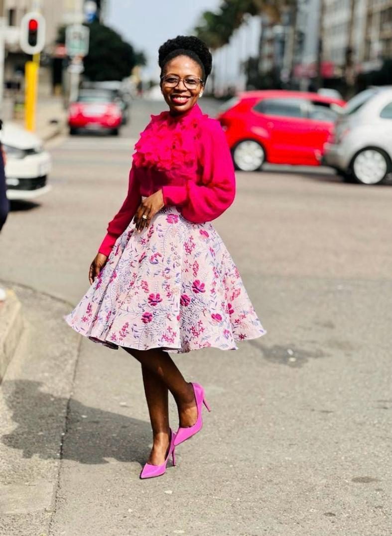 Smiling woman in a hot pink ruffle blouse and full pink floral midi skirt with pink heels