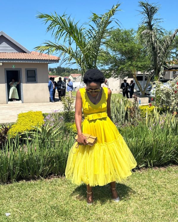 Woman in a sleeveless yellow V-neck dress with bow belt and full tulle midi skirt in a garden